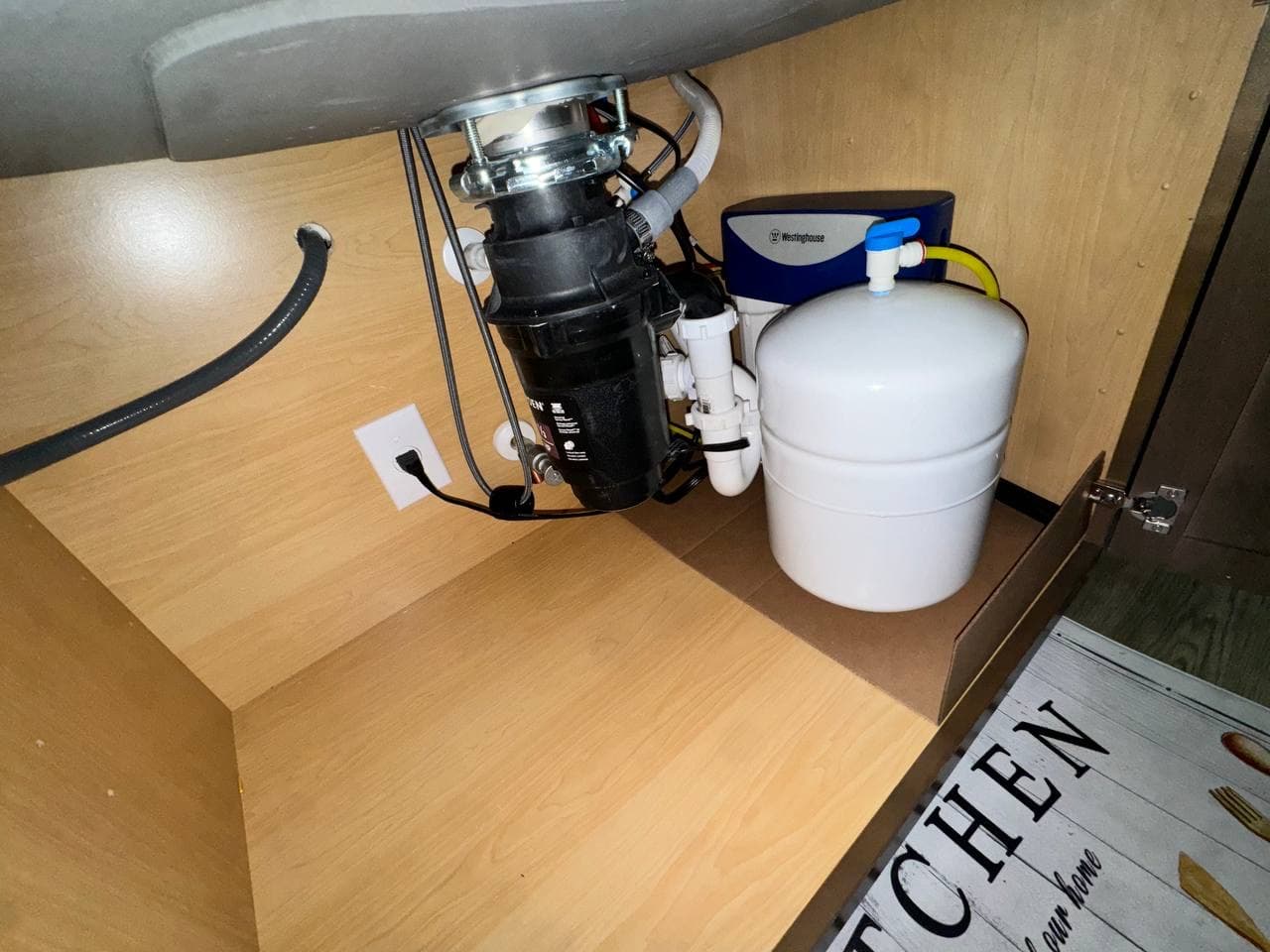 Clean under-sink drinking water filtration setup with storage tank.