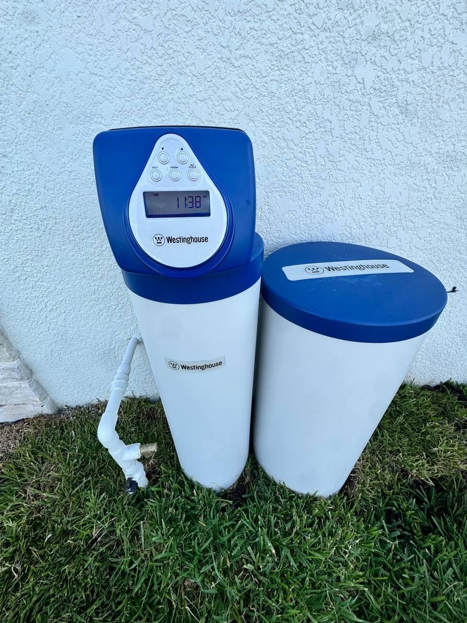 Outdoor whole-home water filtration tanks against a stucco wall.